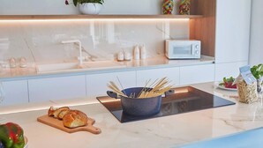 Una cocina moderna con encimera de mármol, una olla de espagueti, una tabla de cortar con pan y un microondas.