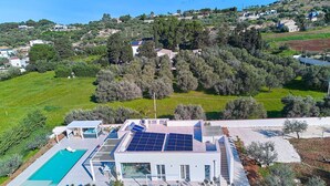 Una casa moderna con piscina, paneles solares y vistas del paisaje circundante.