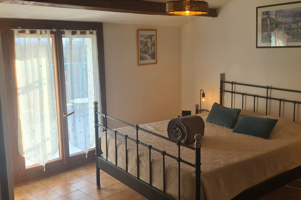 Ein Schlafzimmer mit Bett, Vorhängen, einem Bild an der Wand und einer Nachttischlampe.