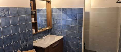 Un baño con lavabo, espejo y repisas con artículos de aseo.