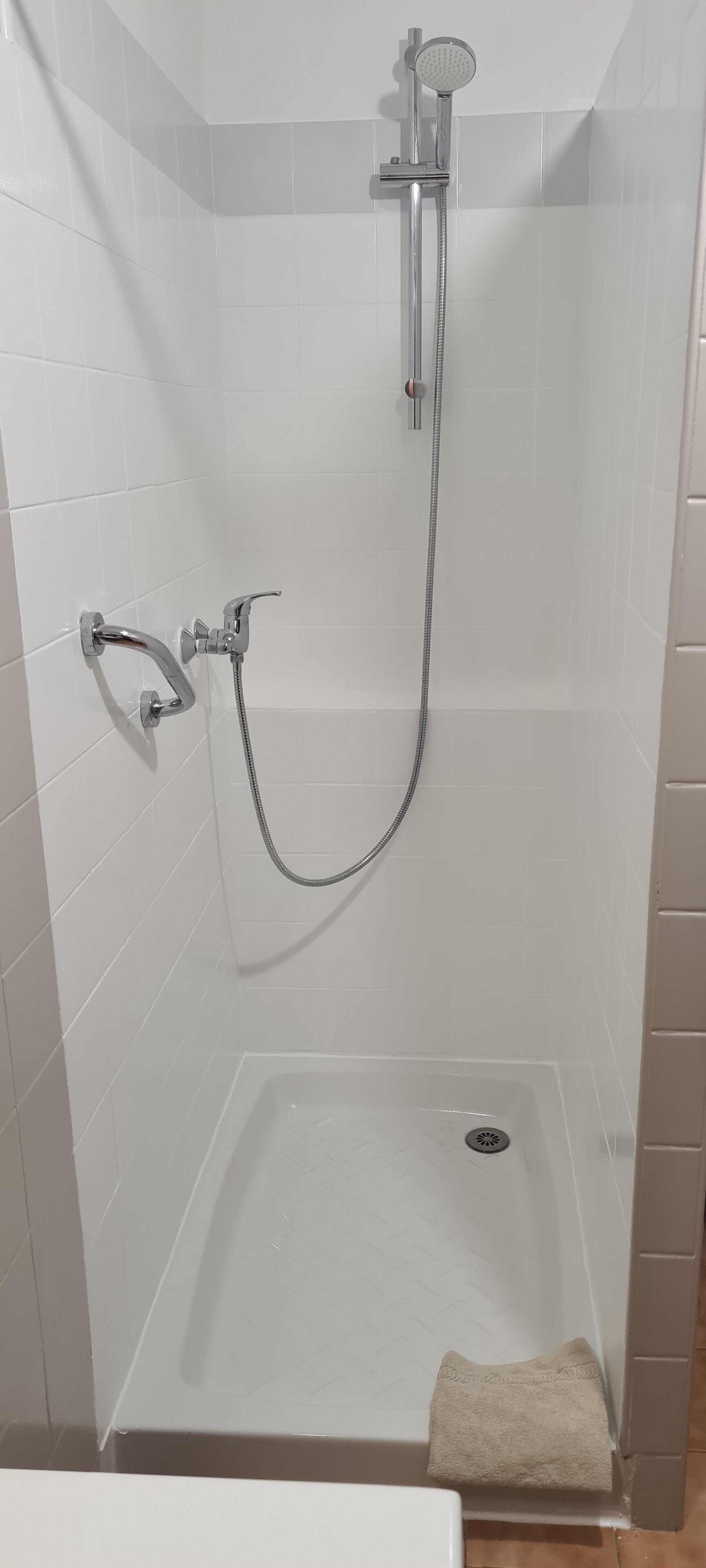 Een douche met een handdouche en een vastgelegde douchekop, een handdoek op de vloer en een afvoer in de douchebak.