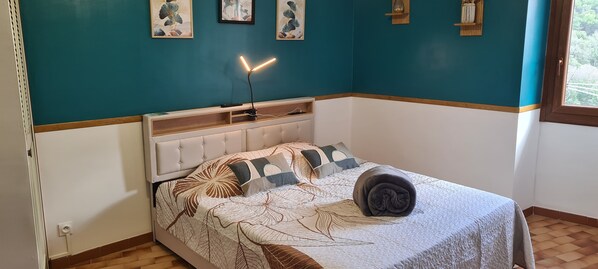 A bedroom with a bed, a bedside table, a lamp, and artwork on the wall.
