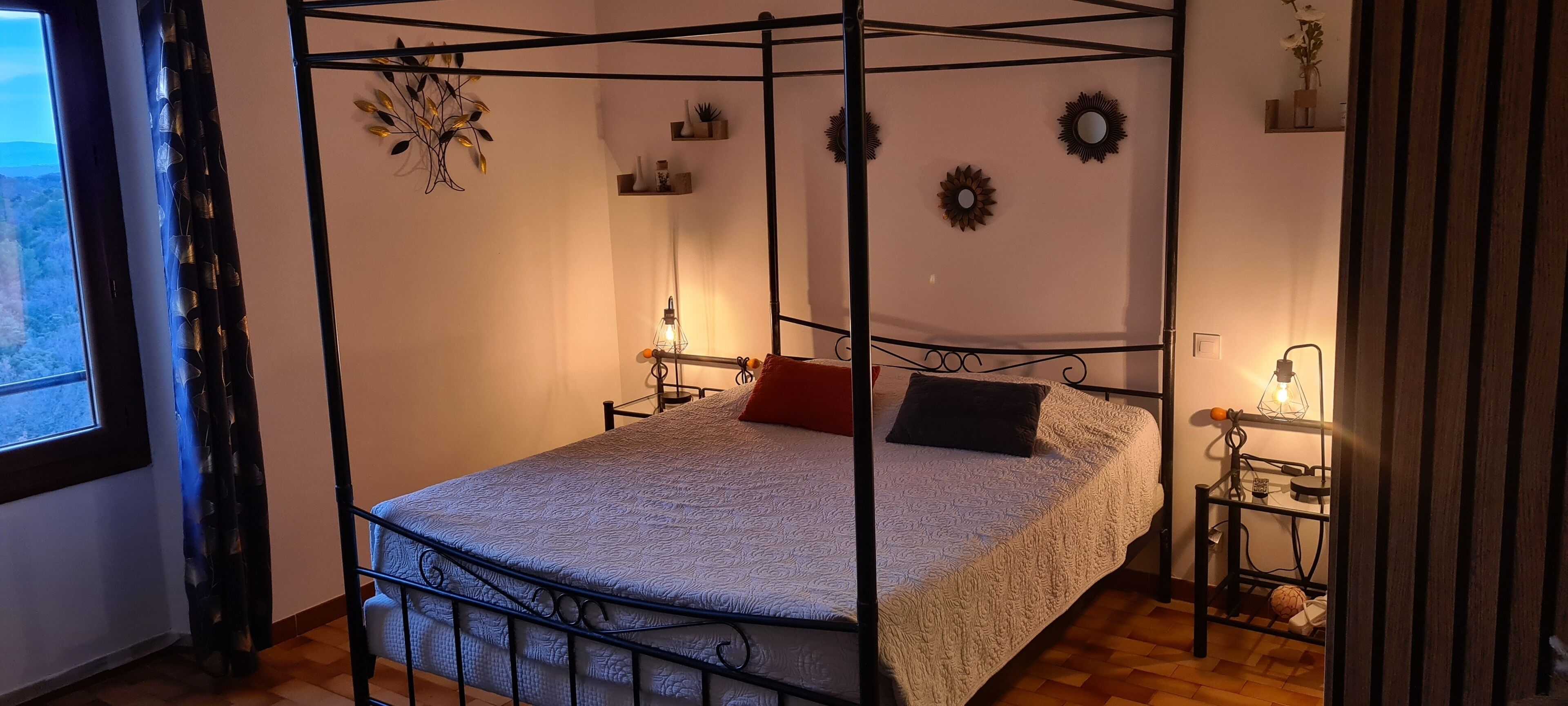 A four-poster bed with a patterned bedspread, two pillows, and bedside lamps.