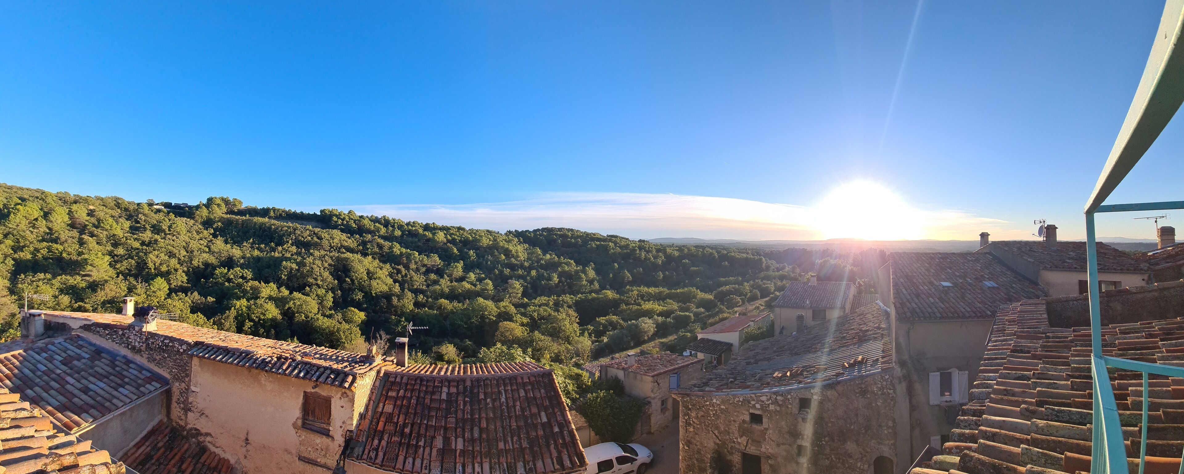 A view of a village with terracotta-roofed buildings and a lush green hillside.