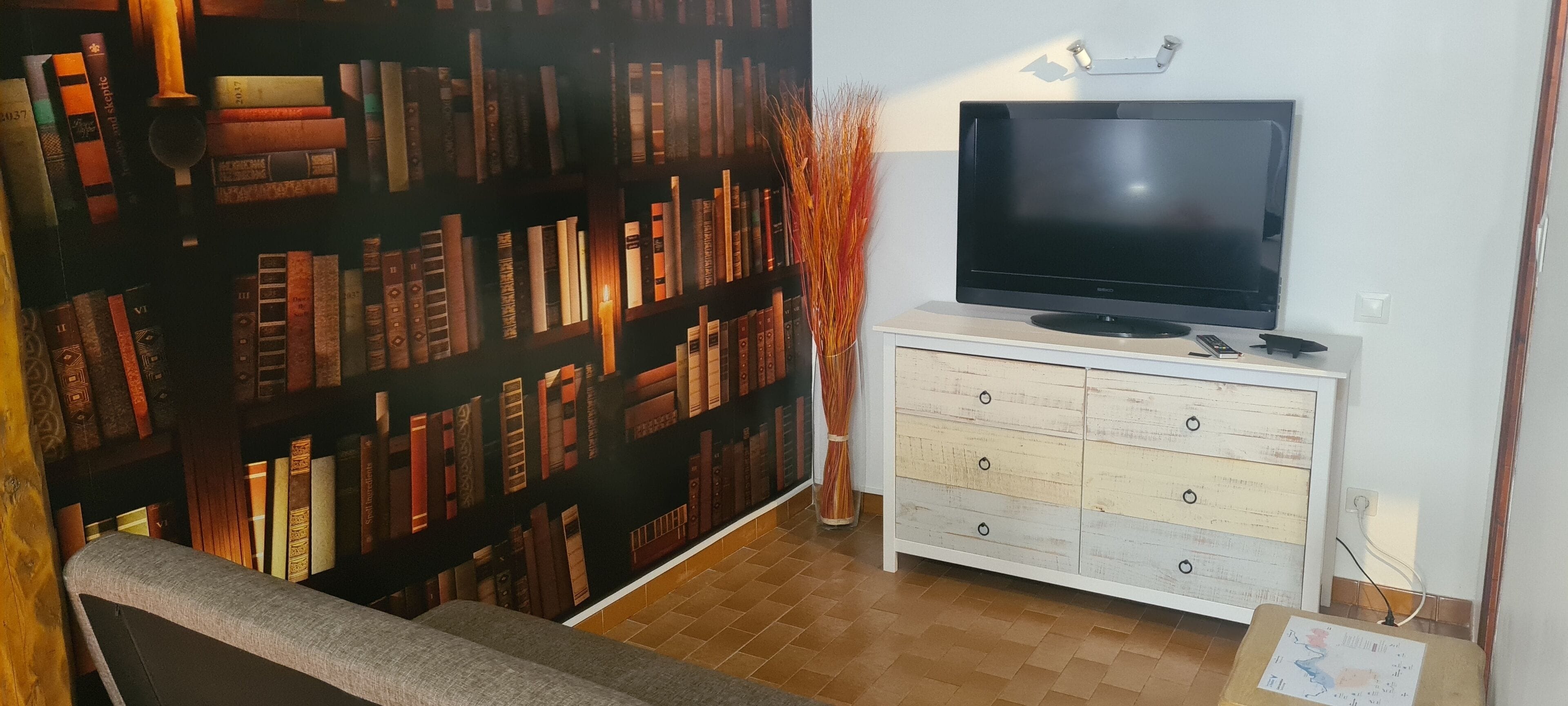 Una stanza con una libreria piena di libri, un televisore su un comò bianco e un tavolino con una mappa.
