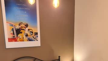 Una cama bien hecha con una toalla enrollada, un cartel enmarcado en la pared y una lámpara de noche.