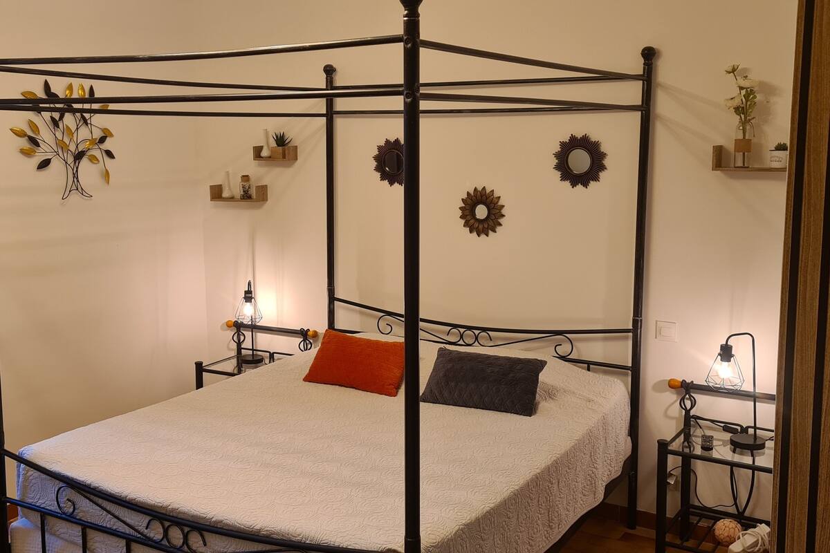 Ein Himmelbett mit weißer Bettdecke und zwei Kissen, flankiert von Nachttischen mit Lampen und Dekorationselementen.