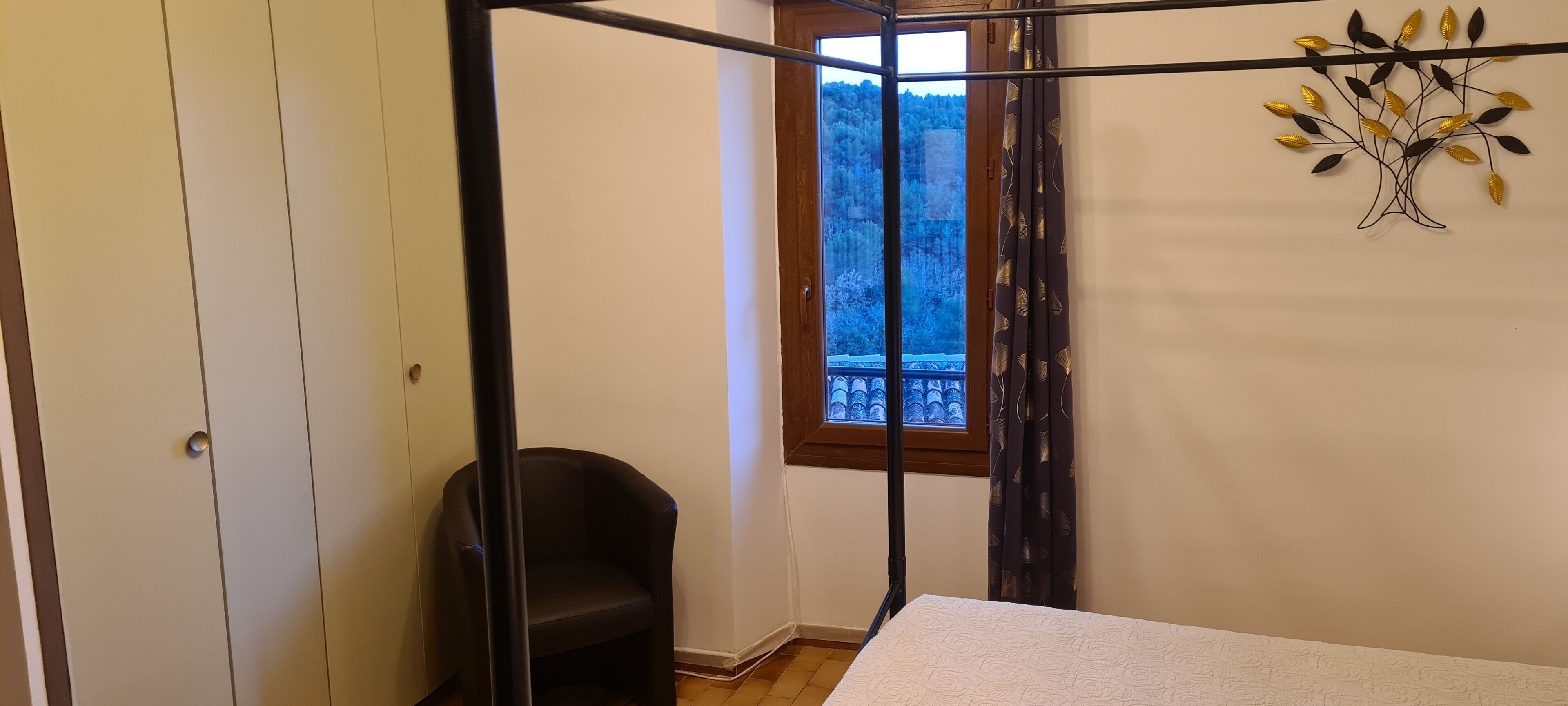 A bedroom with a bed, a chair, a window with a view of trees, and a wall decoration.