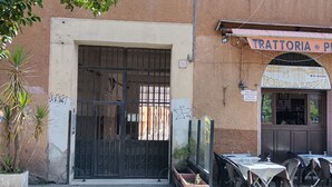 A building with a large metal gate, outdoor seating with tables and chairs, and a sign above the entrance. - Cozy studio apartment with loft in San Lorenzo (Roma)