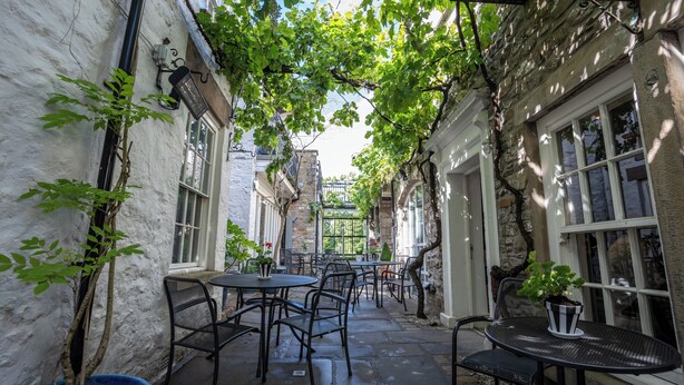 An outdoor café with tables and chairs, surrounded by stone walls and greenery. - Plato's (Kirkby Lonsdale)