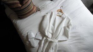 A neatly arranged white bathrobe and slippers on a bed with a textured pillow.