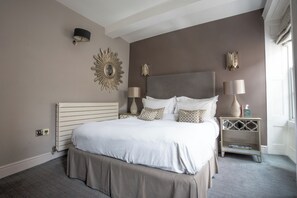 A neatly arranged bedroom with a large bed, two bedside lamps, a decorative wall piece, and a nightstand with a vase.