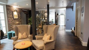A spacious lobby with two armchairs, a small wooden table, and a potted plant. - Plato's (Kirkby Lonsdale)