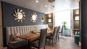 A modern dining area with a wooden table, wicker chairs, and a grey upholstered bench. - Plato's (Kirkby Lonsdale)