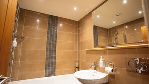 A modern bathroom with a large bathtub, a shower, and a mirror above the sink.