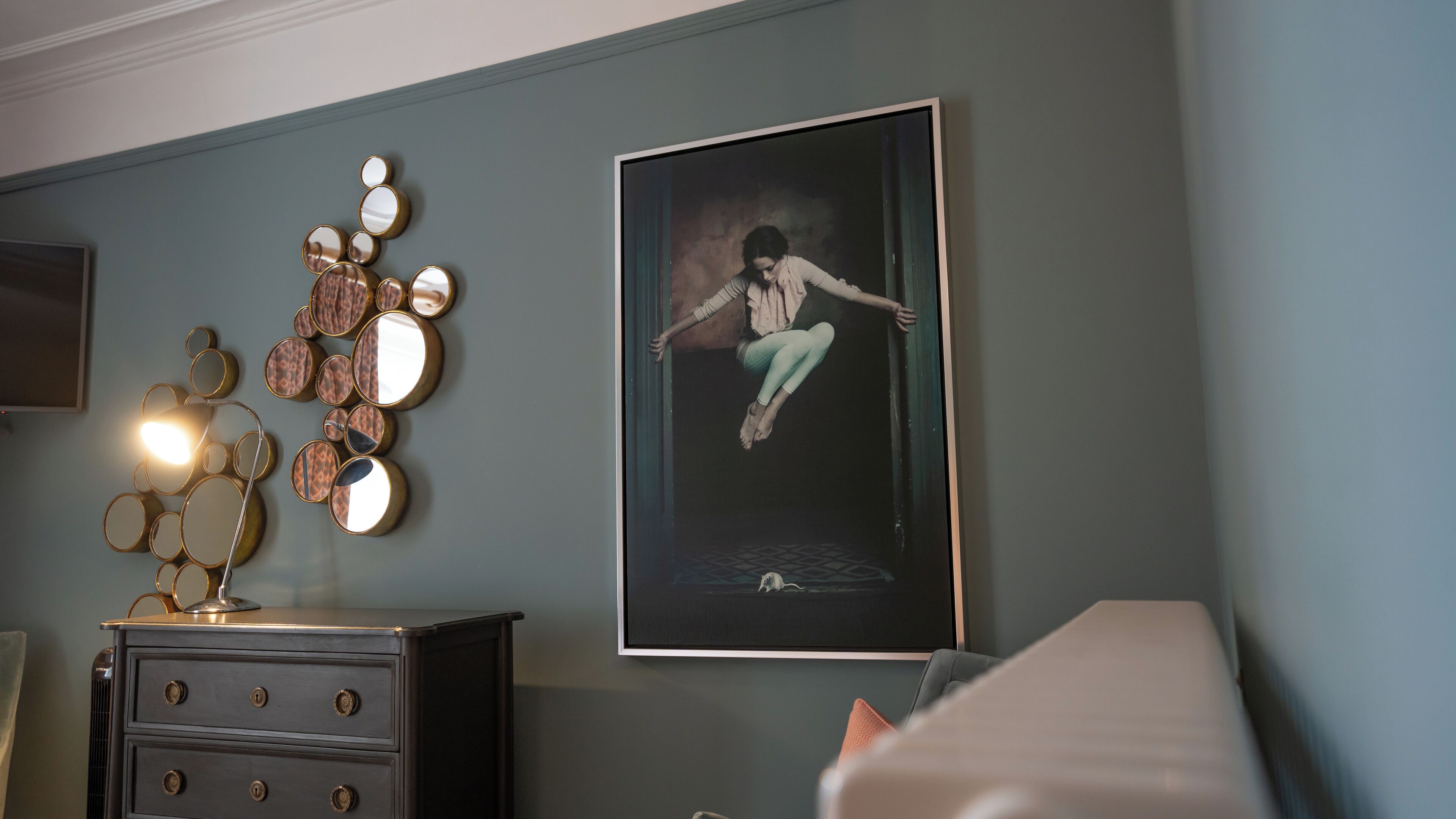 A room with a dark wooden dresser, a wall-mounted mirror arrangement, and a framed picture of a person.