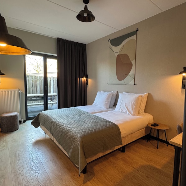 A bedroom with a large bed, a small table, a chair, a radiator, and a view of the outside.