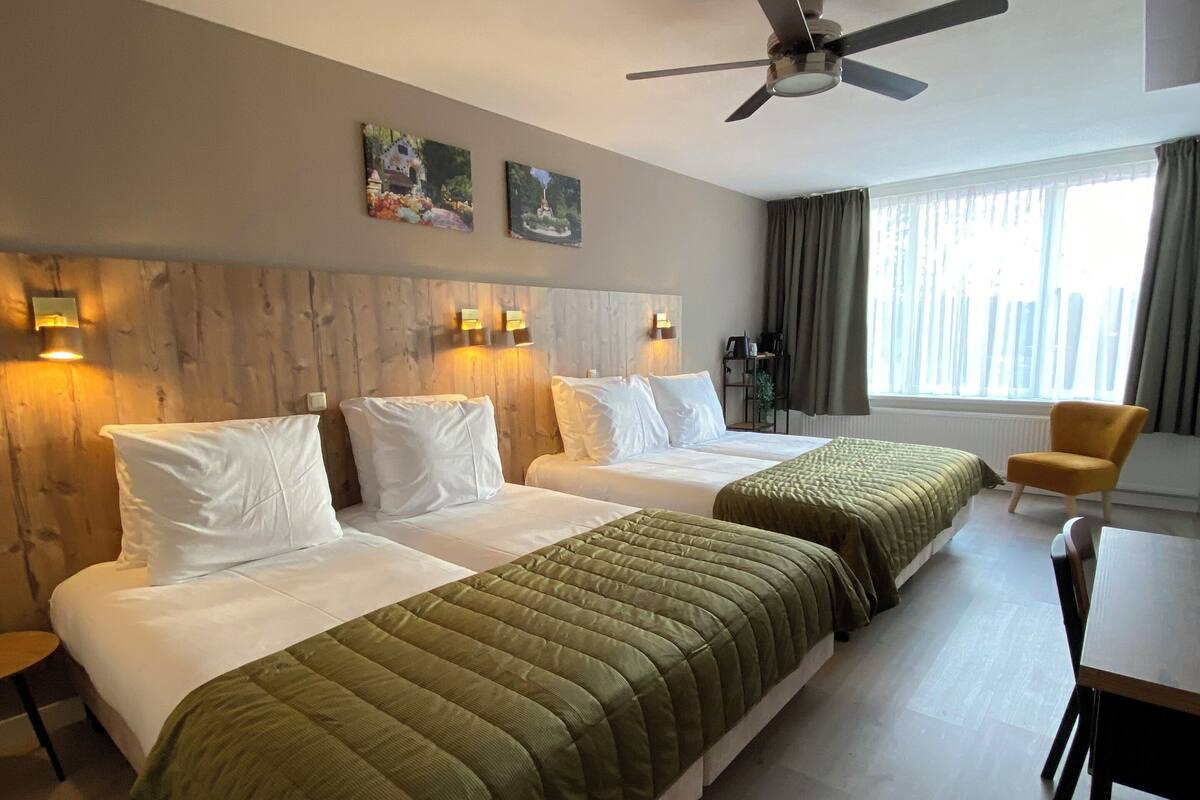Ein Hotelzimmer mit zwei Betten, einem Esstisch, einem Deckenventilator und einem Fenster mit Vorhängen.