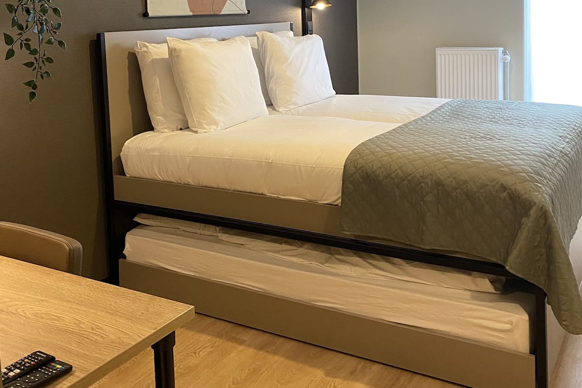 Ein Schlafzimmer mit Bett, Nachttisch, Lampe, Heizkörper und einem Wandbild mit abstrakter Kunst.