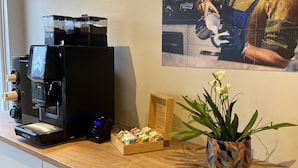 Een koffieapparaat, een houten doos met kaarten, en een bloempot op een aanrecht.