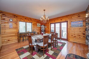 Een houten chalet met een eethoek, inclusief een kroonluchter, een bar en een groot raam.