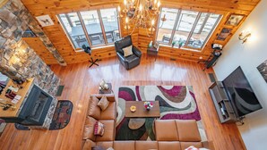 A spacious living room with a large sofa, a coffee table, and a fireplace. There are wooden floors, stone walls, and large windows providing natural light.