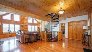 A spacious living area with a wooden floor, a built-in sofa, a dining table, and a spiral staircase.