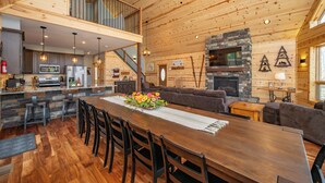 Un vaste espace de vie doté d’un plafond en bois, d’une cheminée en pierre et d’une table à manger avec des chaises.