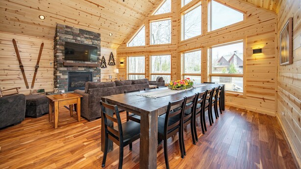 L’intérieur d’un chalet en bois comprend un coin repas, un canapé, une cheminée et de grandes fenêtres.