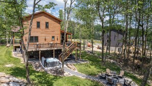 Un chalet en rondins doté d’une terrasse, d’un bain à remous et d’un espace salon extérieur, le tout entouré d’arbres.