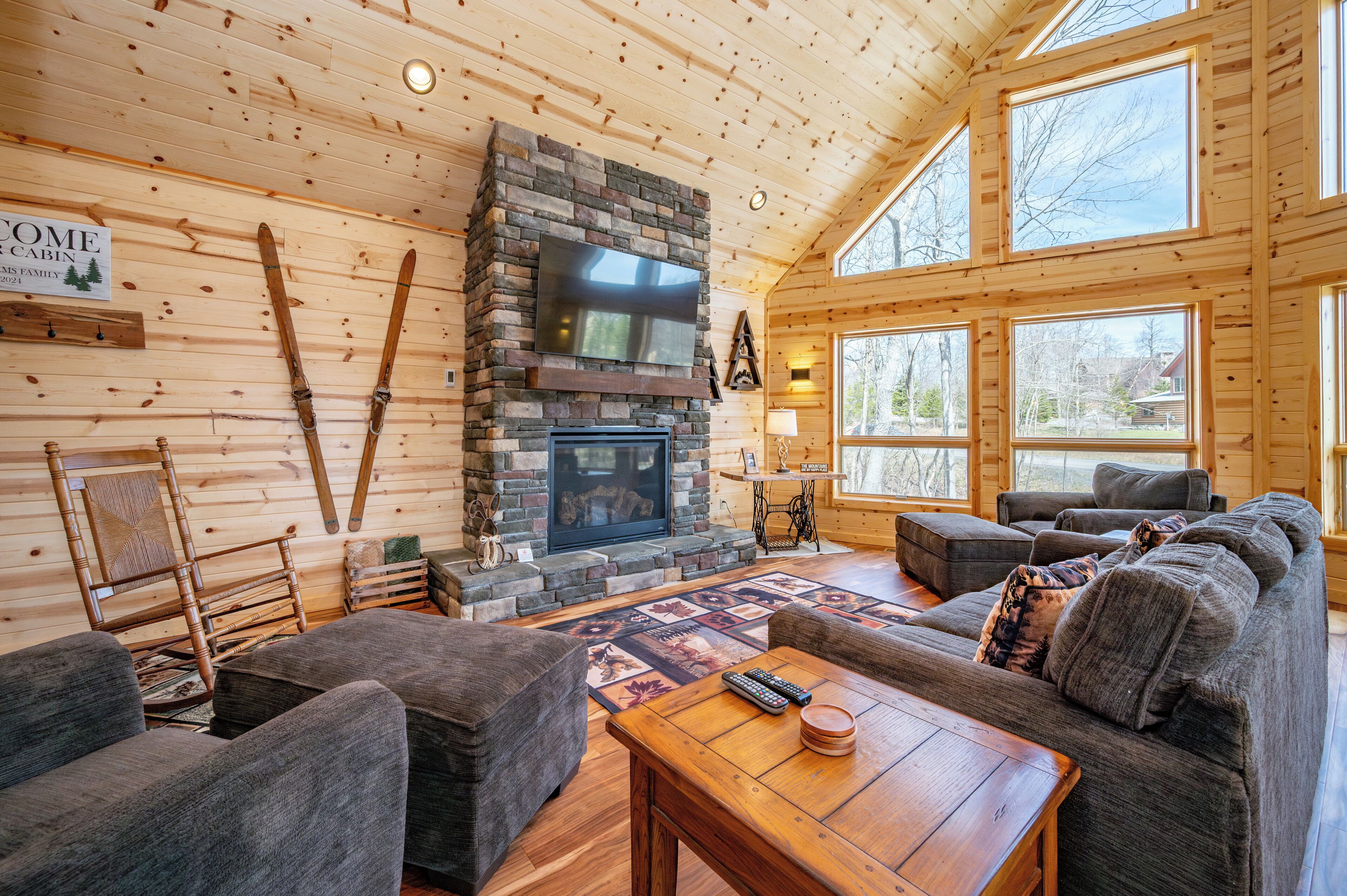 A cozy cabin interior with a stone fireplace, wooden walls, and large windows.