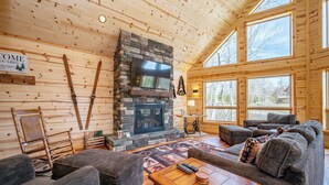 Un intérieur de chalet chaleureux avec une cheminée en pierre, des murs en bois et de grandes fenêtres.
