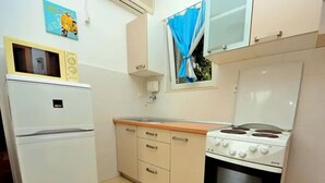 A compact kitchen with a refrigerator, stove, and a window with blue curtains. - Coastal Breeze House (Selca)