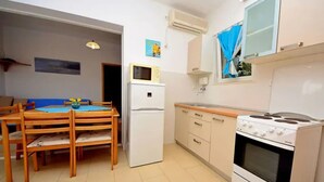 A compact kitchen with a dining area, including a refrigerator, stove, and microwave. - Coastal Breeze House (Selca)