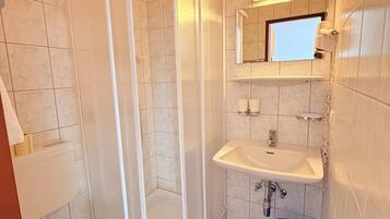 A bathroom with a toilet, a shower enclosure, a sink, and a blue bucket.