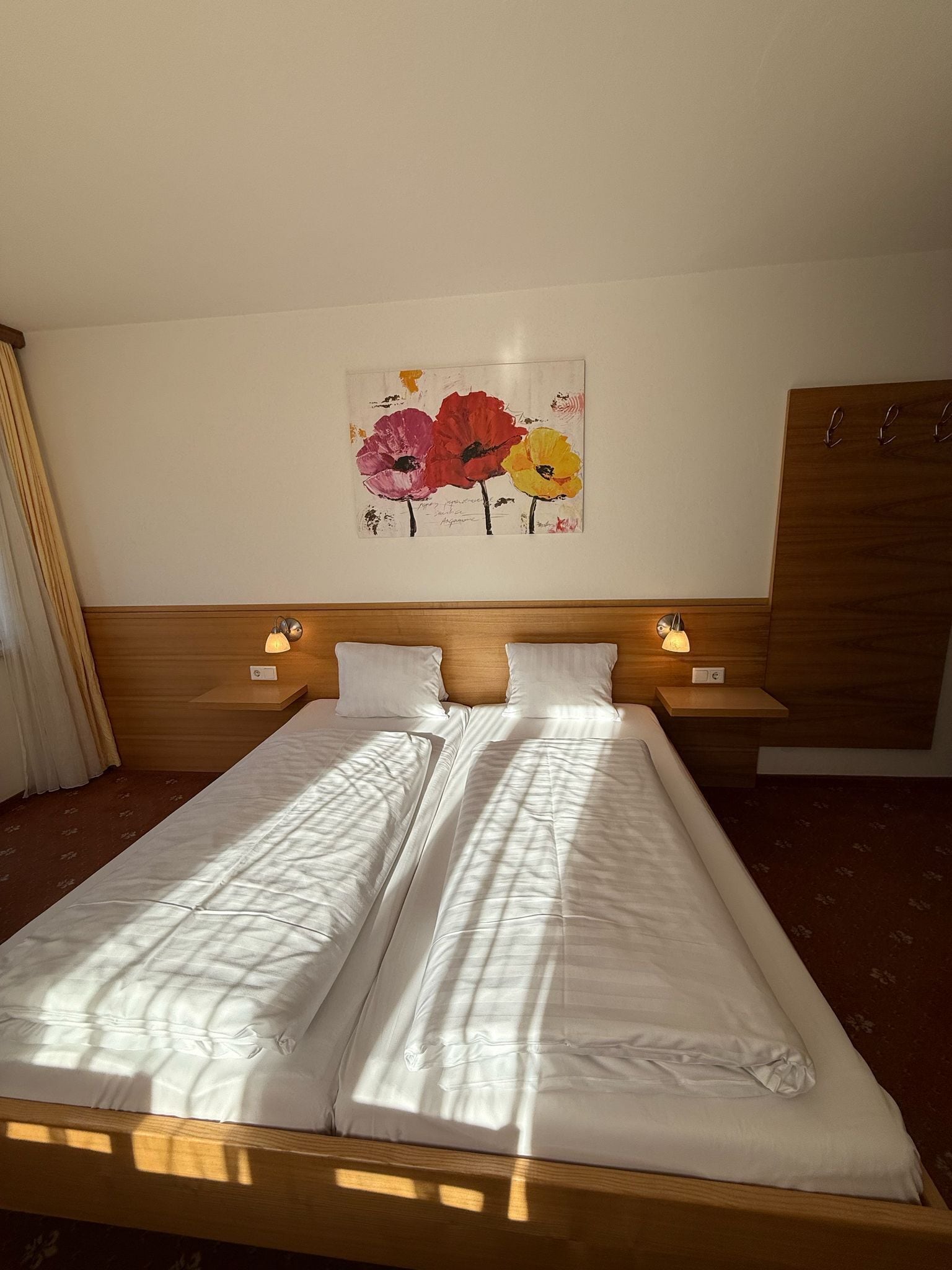 Una cama doble con ropa de cama blanca, dos mesitas de noche con lámparas, un cabecero de madera y un cuadro floral en la pared.