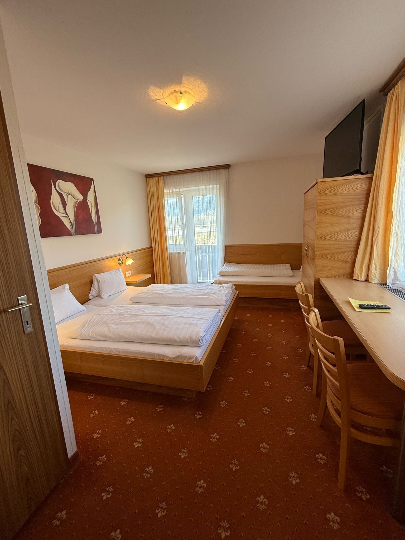 A hotel room with two single beds, a wooden desk, a chair, a TV, and a painting on the wall.