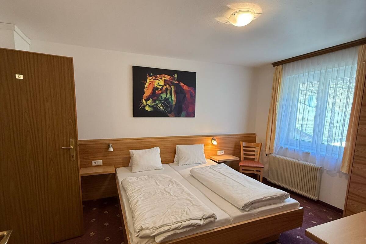 A hotel room with a large bed, a wooden headboard, a painting of a tiger, a desk, and a chair.
