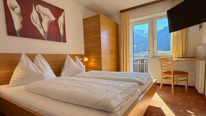 A hotel room with a large bed, a wooden wardrobe, a desk with a chair, a television, and a painting on the wall. - Pension Plattenhof  (Telfs)