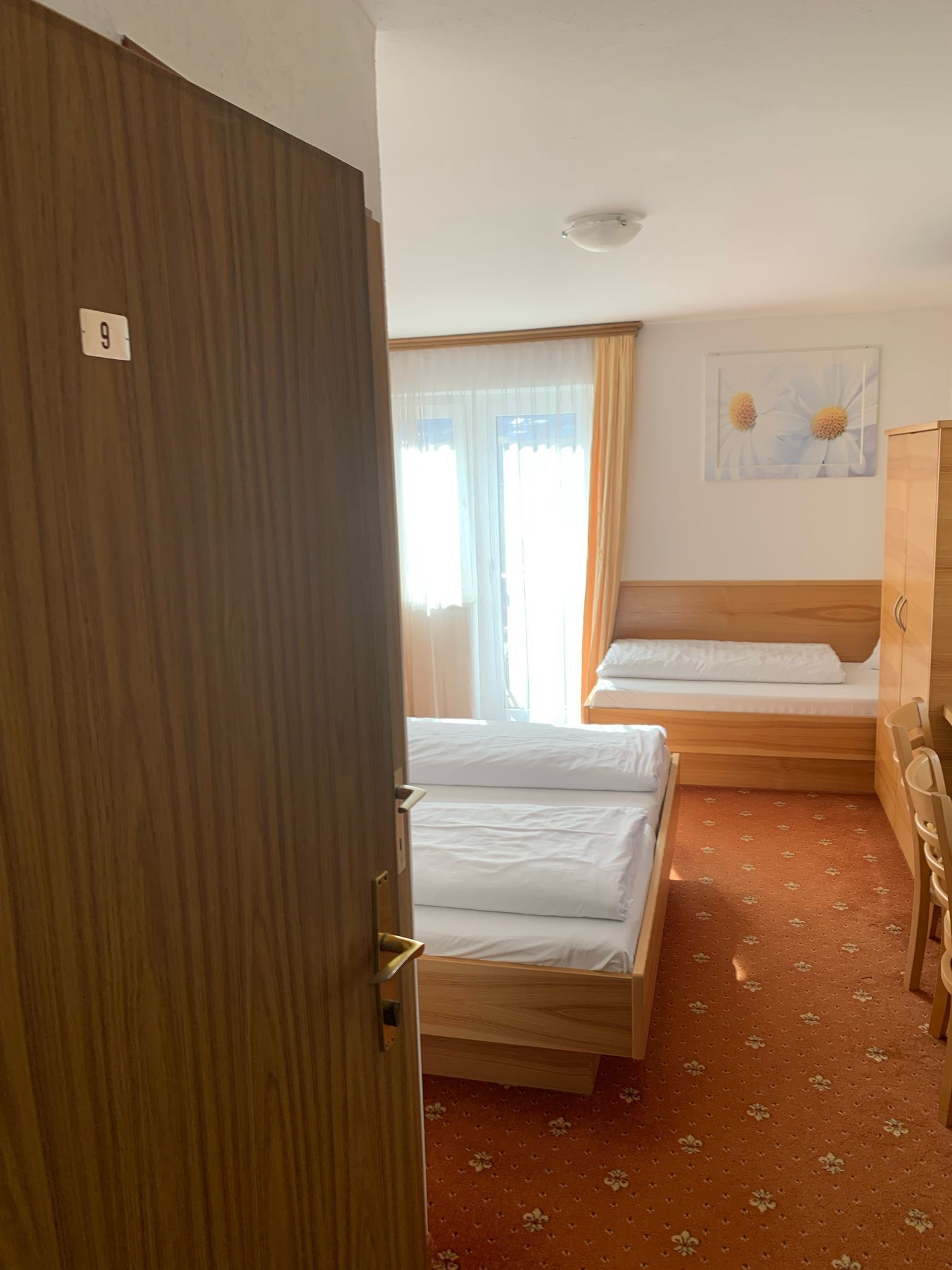 Habitación de hotel con dos camas, un armario de madera, un escritorio y una ventana con cortinas.