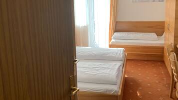 Habitación de hotel con dos camas, un armario de madera, un escritorio y una ventana con cortinas.