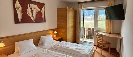 Een hotelkamer met een groot bed, een bureau met stoel, een televisie en een schilderij aan de muur.