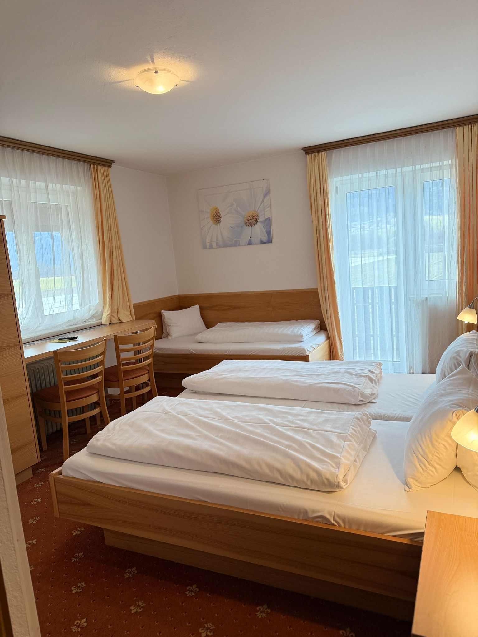 Camera d'albergo con due letti singoli, una scrivania in legno con una sedia e un termosifone.
