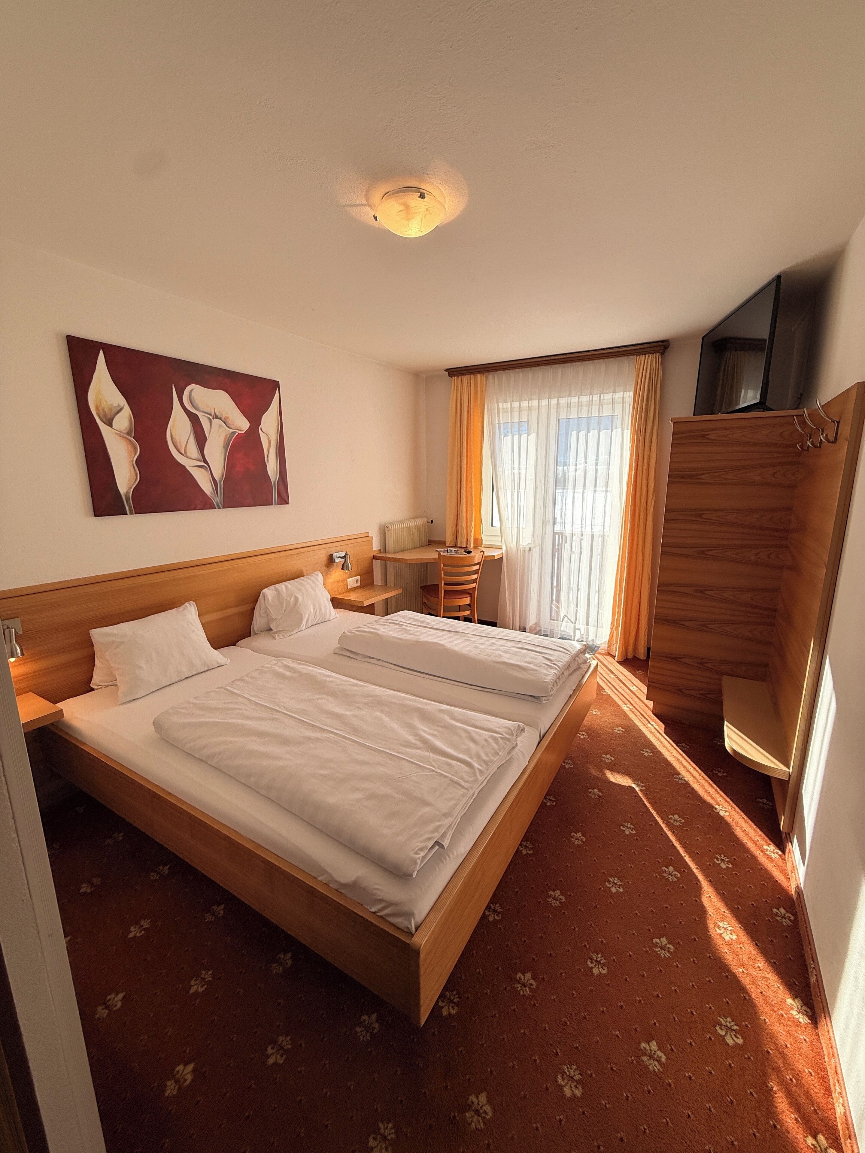 Ein Hotelzimmer mit einem großen Bett, einem Schreibtisch, einem Sessel, einer Heizung und einem Bild an der Wand.