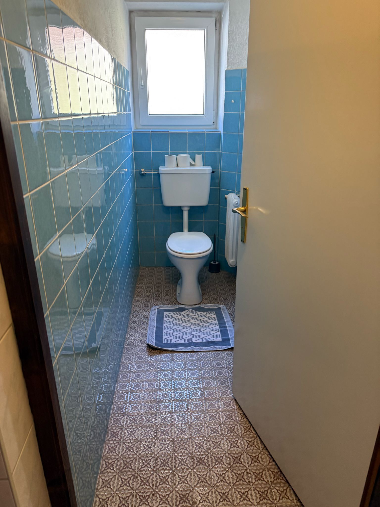 A small bathroom with a toilet, a window, and patterned tiles.