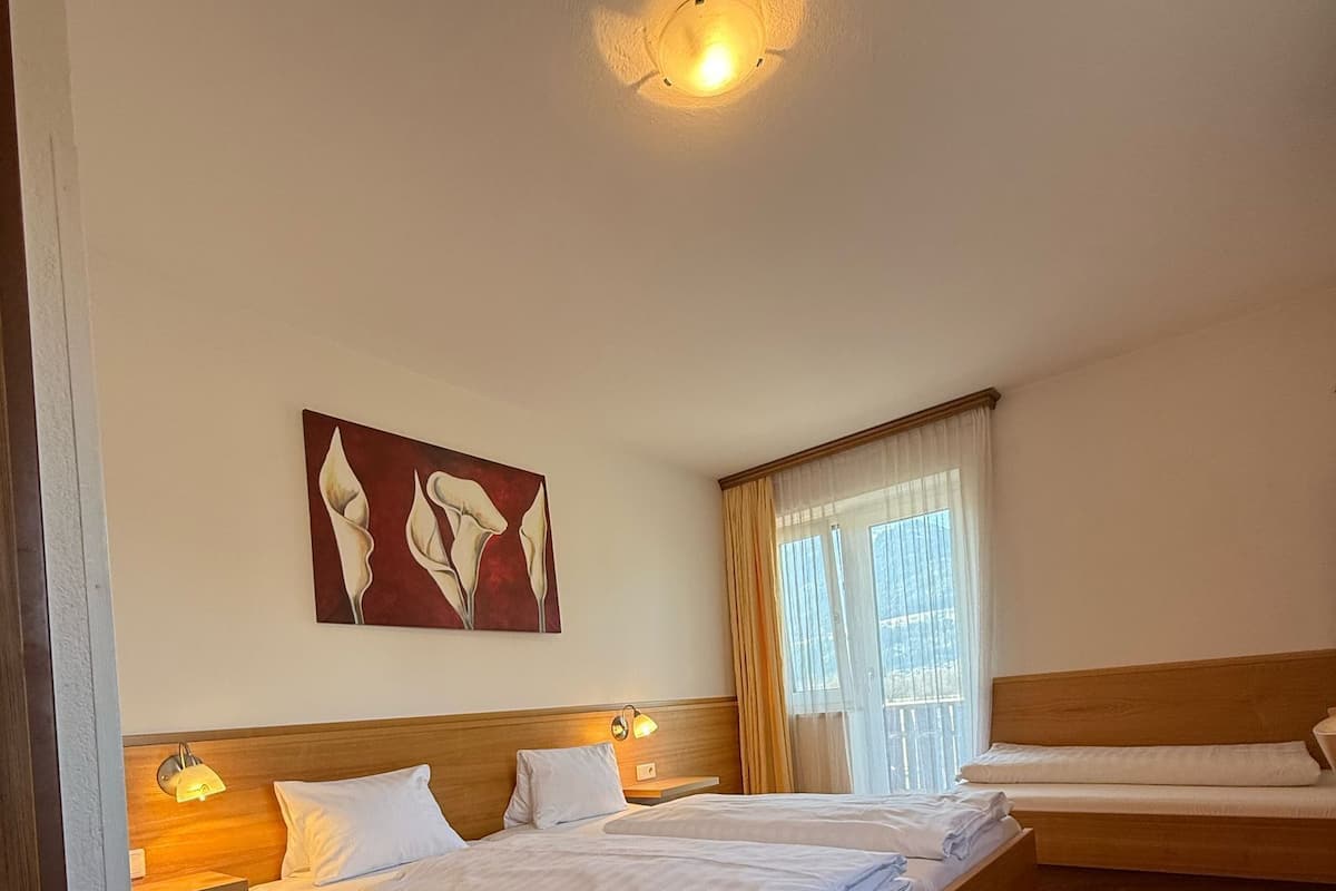 A hotel room with a large bed, a smaller bed, a painting on the wall, and a window with curtains.