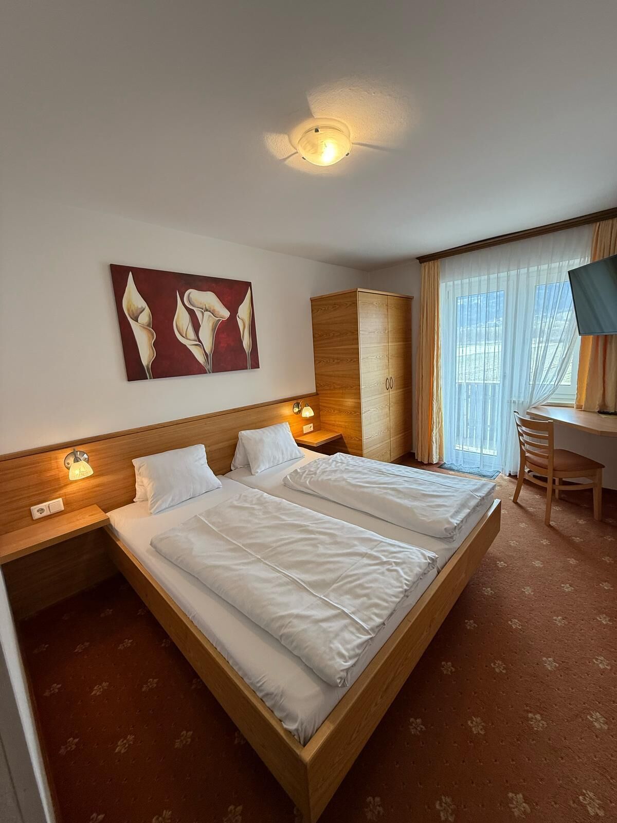 Une chambre d’hôtel avec deux lits, une tête de lit en bois, un tableau, une armoire, un bureau avec une chaise et un téléviseur.