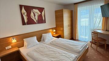 Une chambre d’hôtel avec deux lits, une tête de lit en bois, un tableau, une armoire, un bureau avec une chaise et un téléviseur.