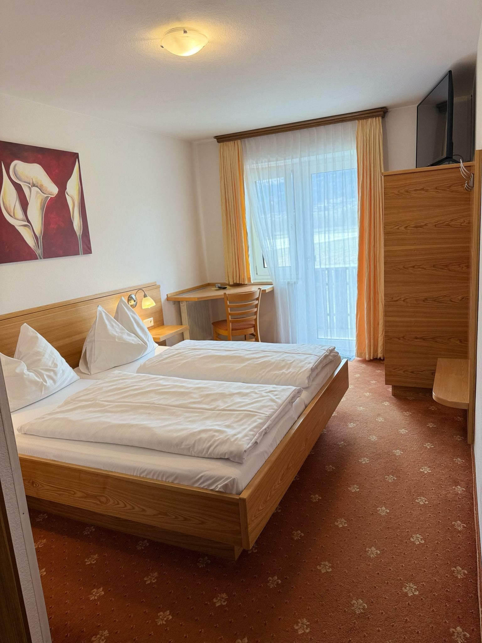 Une chambre d’hôtel avec un lit, un bureau, une chaise, une armoire et un tableau au mur.