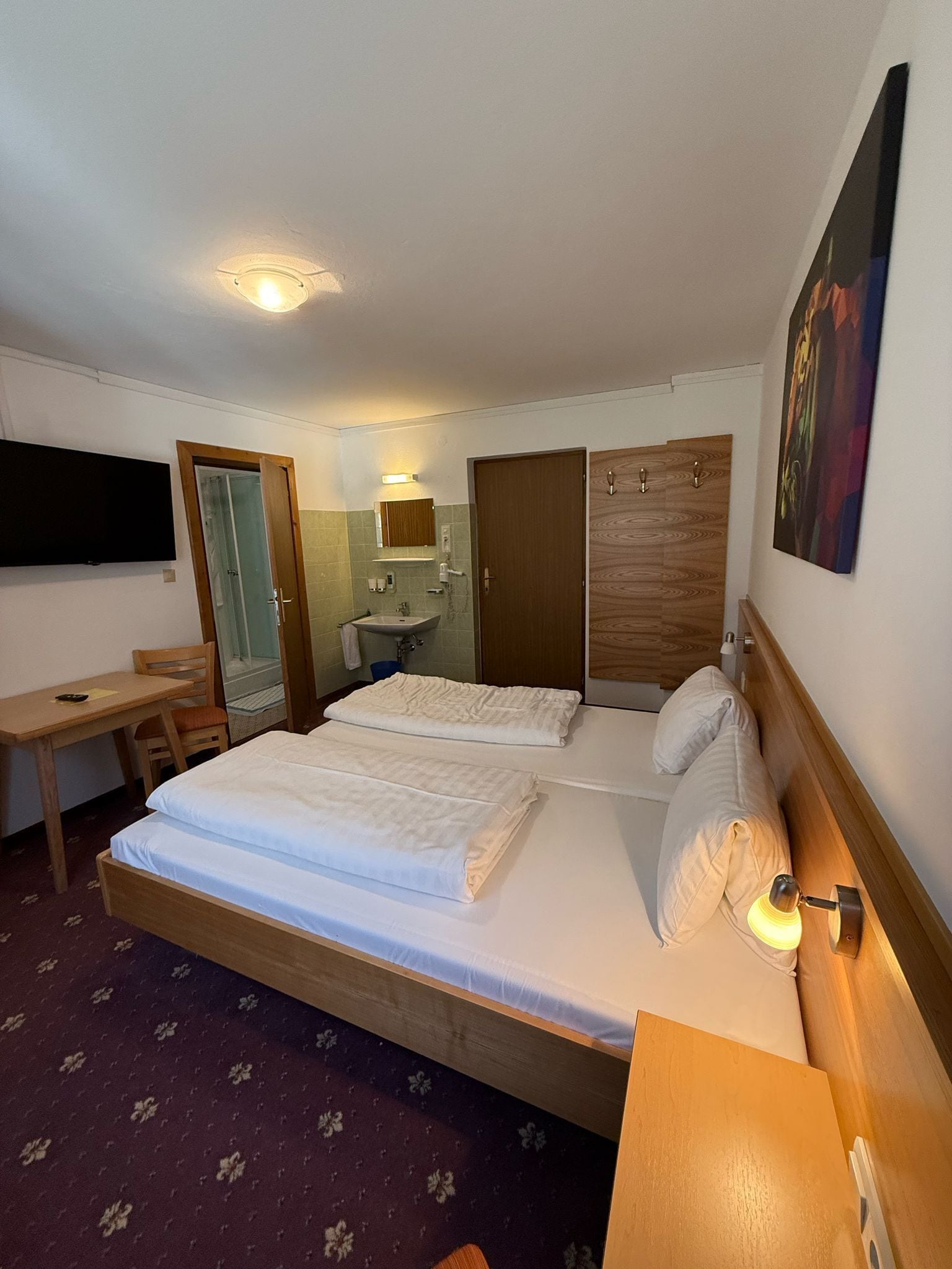 Habitación de hotel con dos camas, un escritorio, un espejo, un armario de madera y un televisor en la pared.
